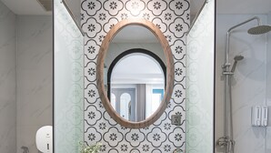 Un baño con tocador de madera, espejo redondo, inodoro y ducha.