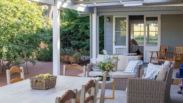 Un patio al aire libre con mobiliario de mimbre, una mesa con una cesta de fruta y vistas al jardín.