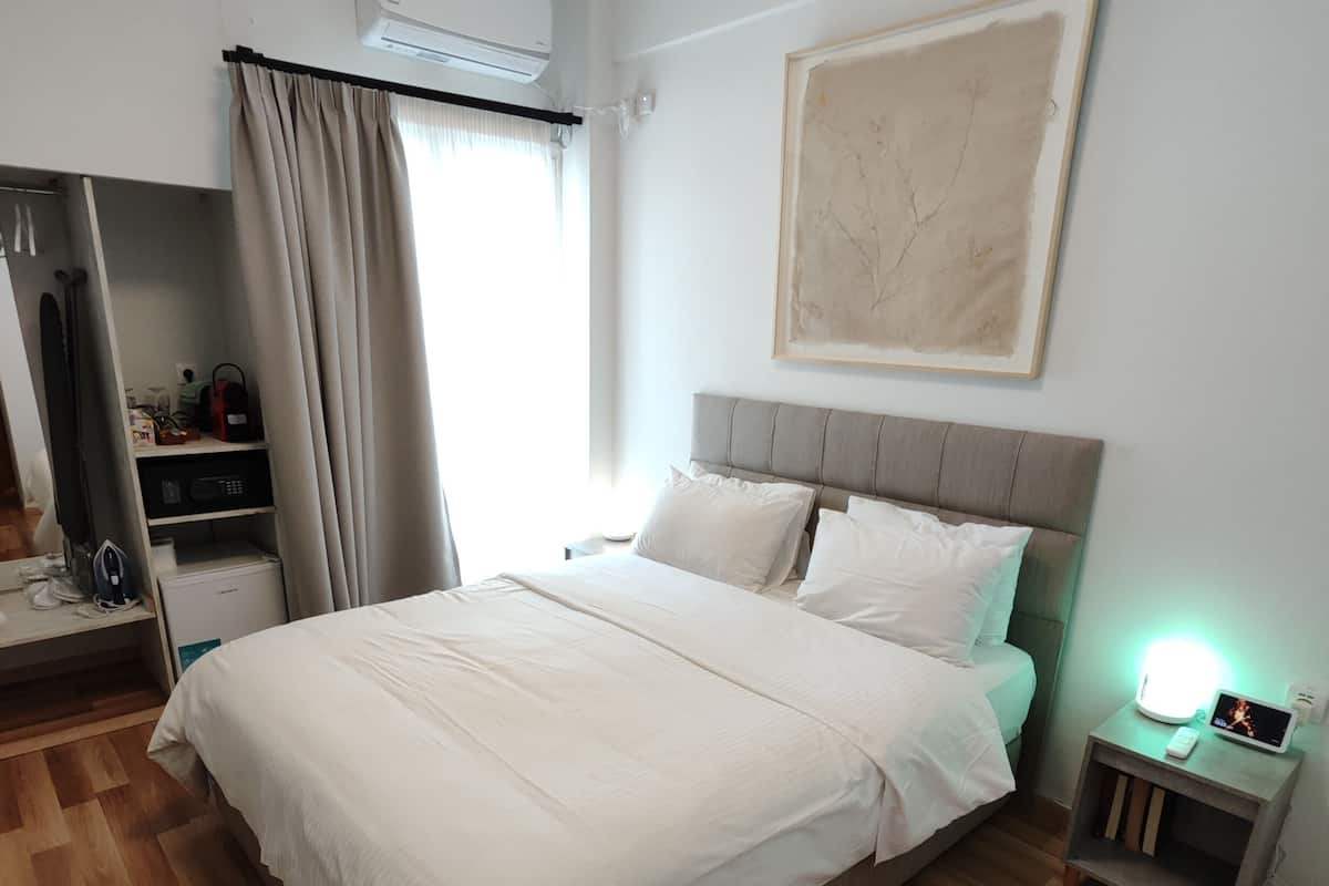 A neatly arranged bedroom with a large bed, a bedside table with a lamp, a wardrobe, and an air conditioning unit.