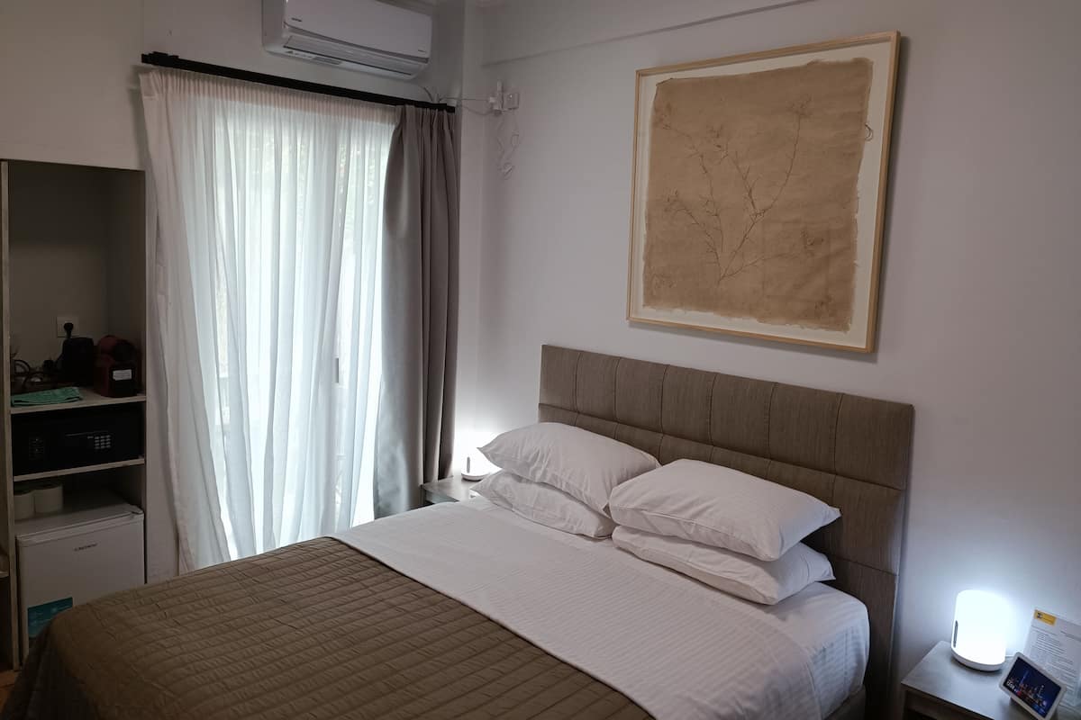A hotel room with a bed, a bedside table with a lamp, a wardrobe, and an air conditioning unit.