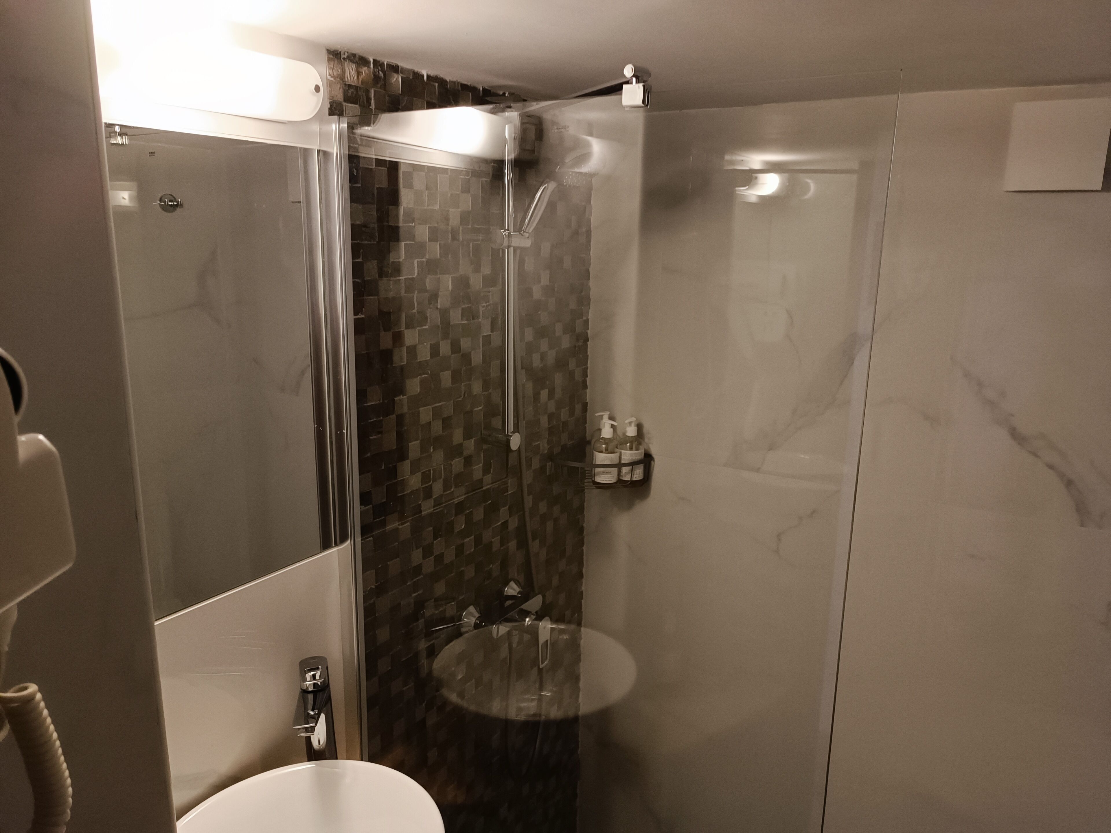Un baño moderno con ducha de vidrio, lavamanos redondo y pared de mármol.