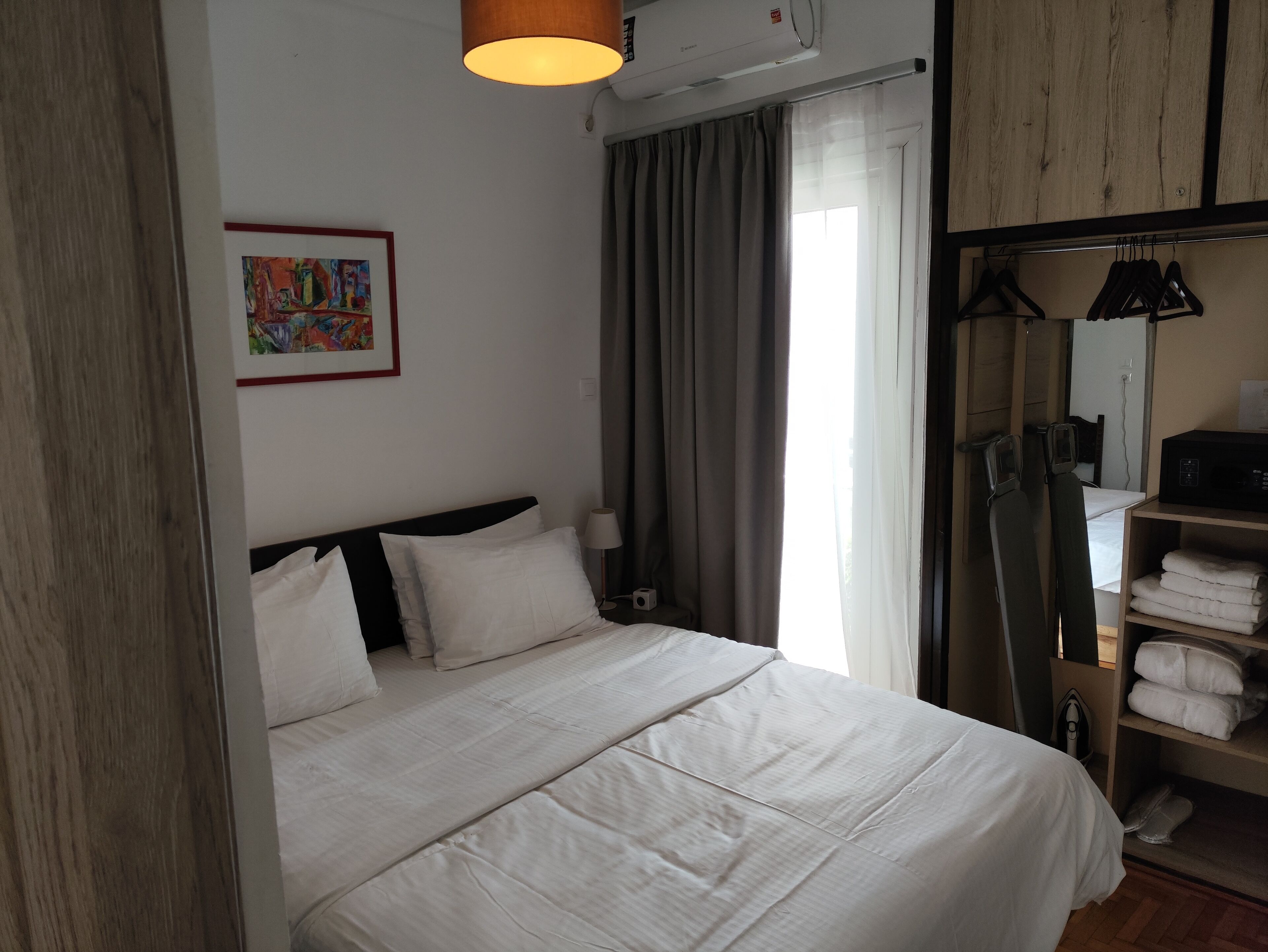Uma cama bem arrumada com lençóis brancos, uma luminária de cabeceira e um quadro na parede.