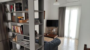 A modern living room with a grey bookshelf, a dark sofa, a flat-screen TV, and a wooden coffee table. - Ulysses Apartments Acropolis (Athens)