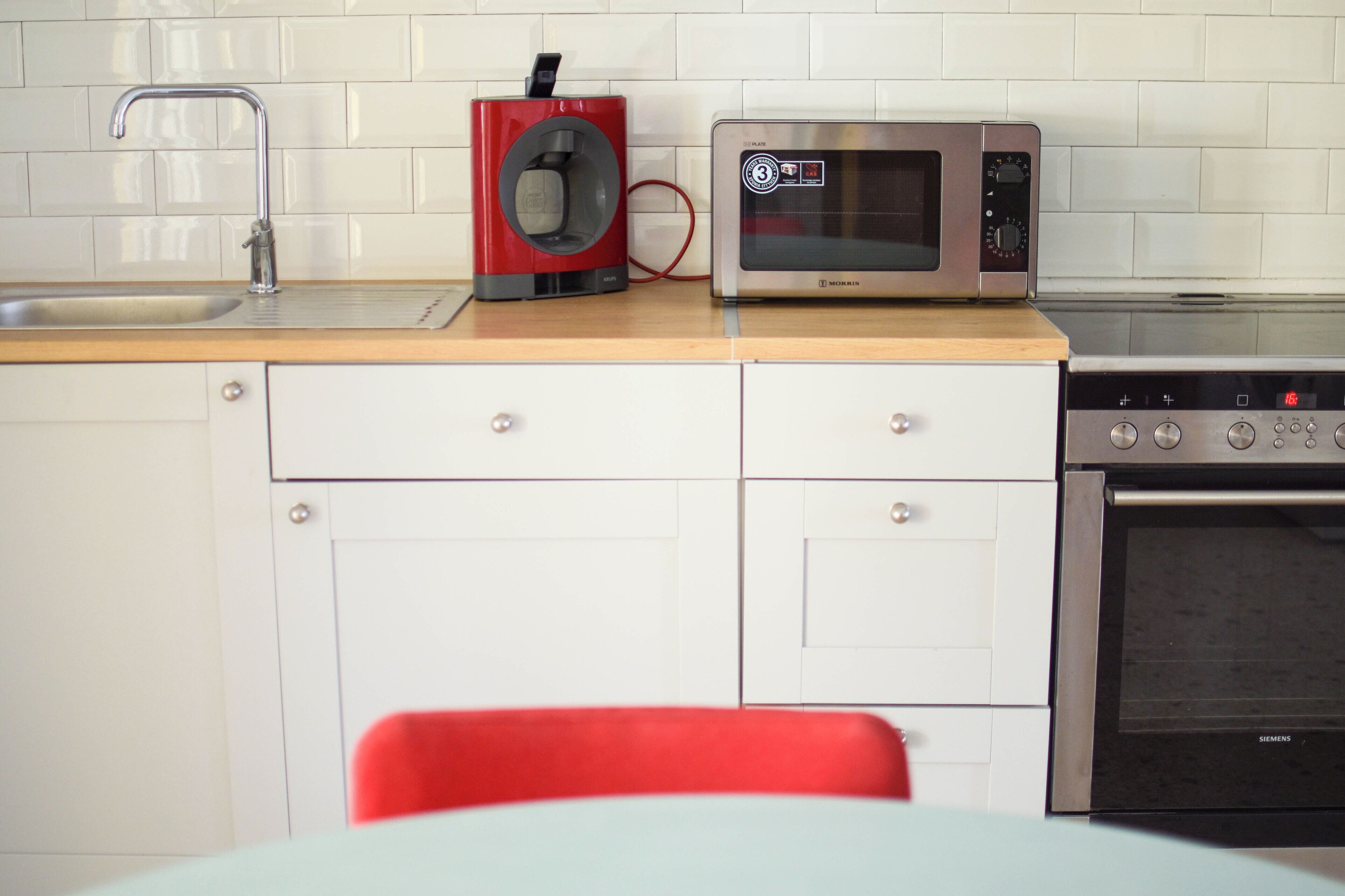 A kitchen with a stainless steel microwave, a red coffee maker, a sink, and a Siemens oven.