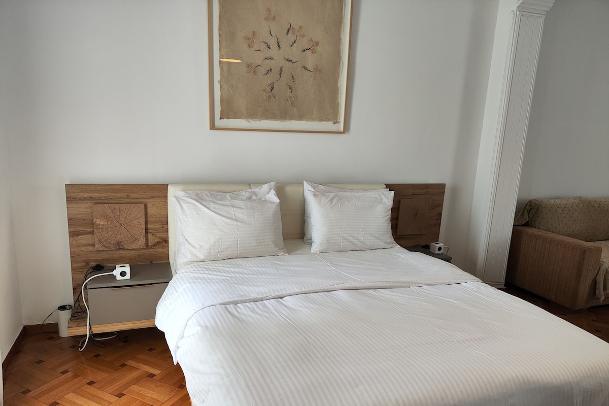 A neatly made bed with white linens, a wooden headboard, and a wall-mounted artwork.