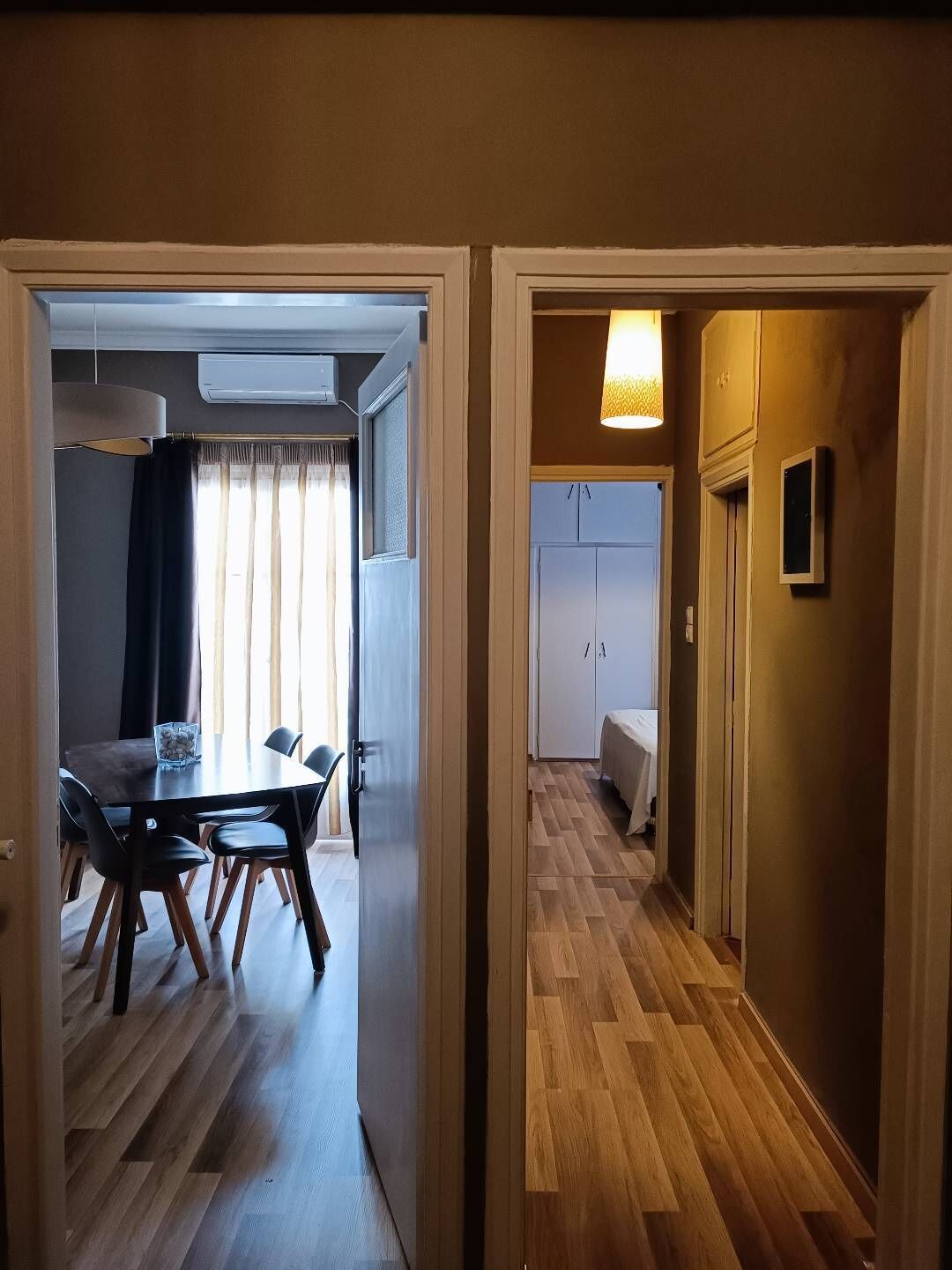 A hallway with wooden flooring leading to a dining area with a table and chairs, and a bedroom with a bed and wardrobe.