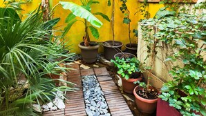 A small, enclosed garden area with potted plants, a wooden pathway, and a yellow wall. - Ulysses Apartments Acropolis (Athens)