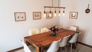 A dining area with a wooden table, white chairs, a vase of flowers, and framed pictures on the wall. - Apt D 016 by Interhome (Disentis)