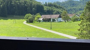 A rural landscape with a winding road, a white building with a red roof, surrounded by green fields and trees.