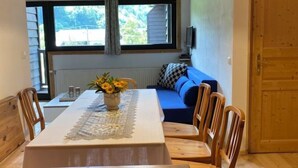 A dining area with a table, chairs, a vase of flowers, a sofa, and a window with a view.