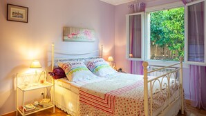 Un dormitorio con cama, lámparas de noche, una ventana con cortinas e imagen colgada en la pared.