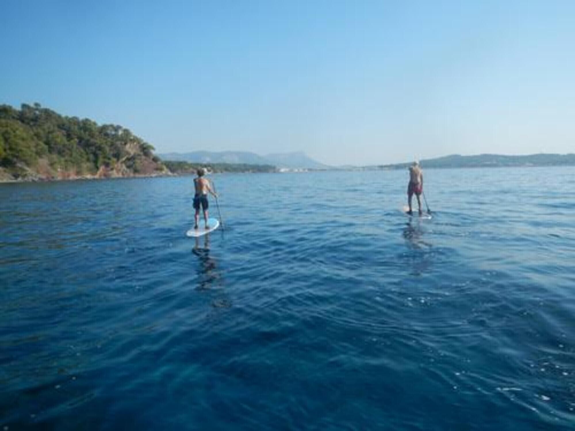 Deux personnes pratiquent le paddle sur une étendue d’eau calme, avec une côte boisée en arrière-plan.
