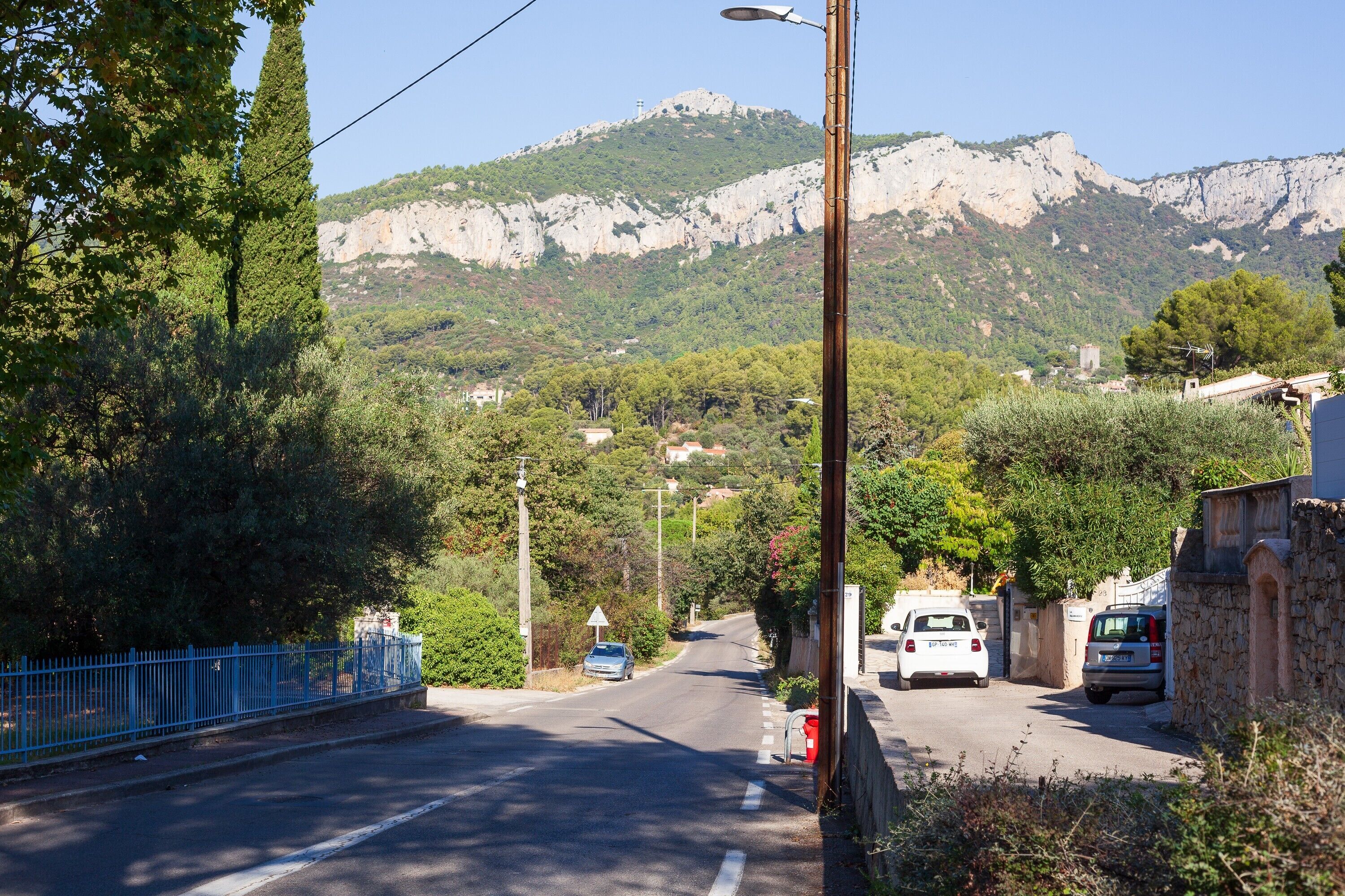 Eine Straße mit Autos, ein blauer Zaun und ein Berg im Hintergrund.