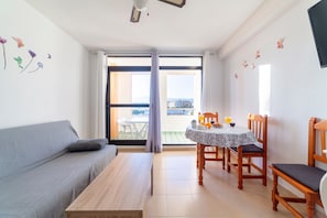 A room with a sofa, a dining table with chairs, a window with curtains, and a view of the outside.