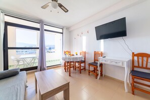 Una habitación con cama, una mesa, un escritorio, una silla, televisor y un balcón con mesa y sillas.