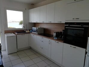 Una cocina con armarios blancos, un horno negro y un ventanal con vista al mar.