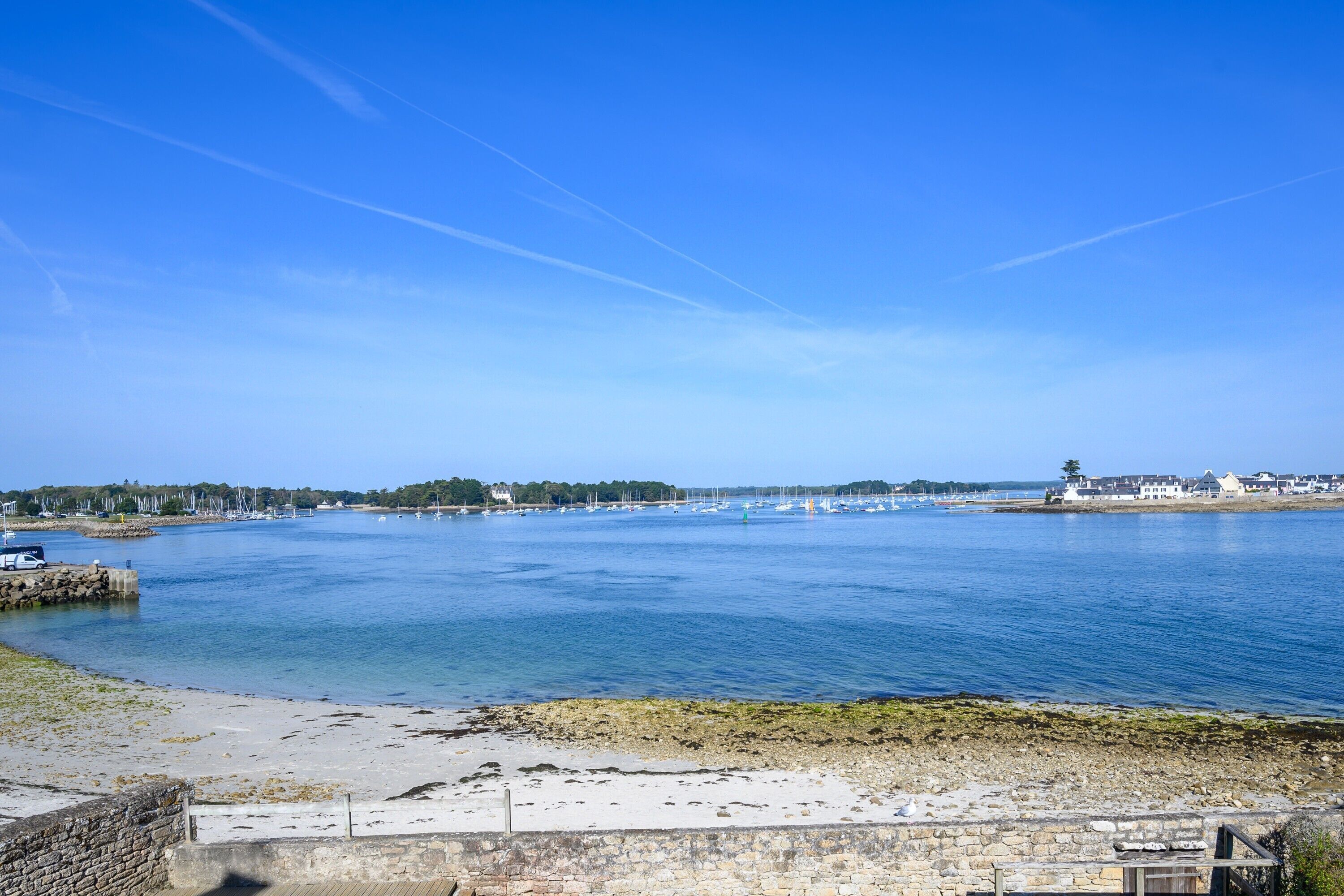 A coastal view with a clear sky, calm water, and a stone wall in the foreground.