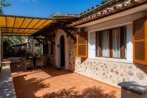 Un patio con mobiliario exterior, un muro de piedra y una zona cubierta con toldo amarillo.