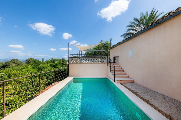 Una piscina con vistas a zonas verdes y montañas, una escalera y una zona con sombra.