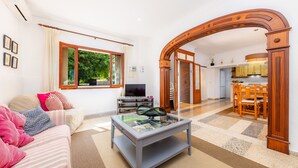 Ein modernes Wohnzimmer mit Sofa, Fernseher und Couchtisch, das in einen Küchenbereich mit Holzmöbeln übergeht.