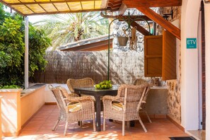 Une terrasse dotée de meubles en osier, une table garnie de fruits et une vue sur la verdure.