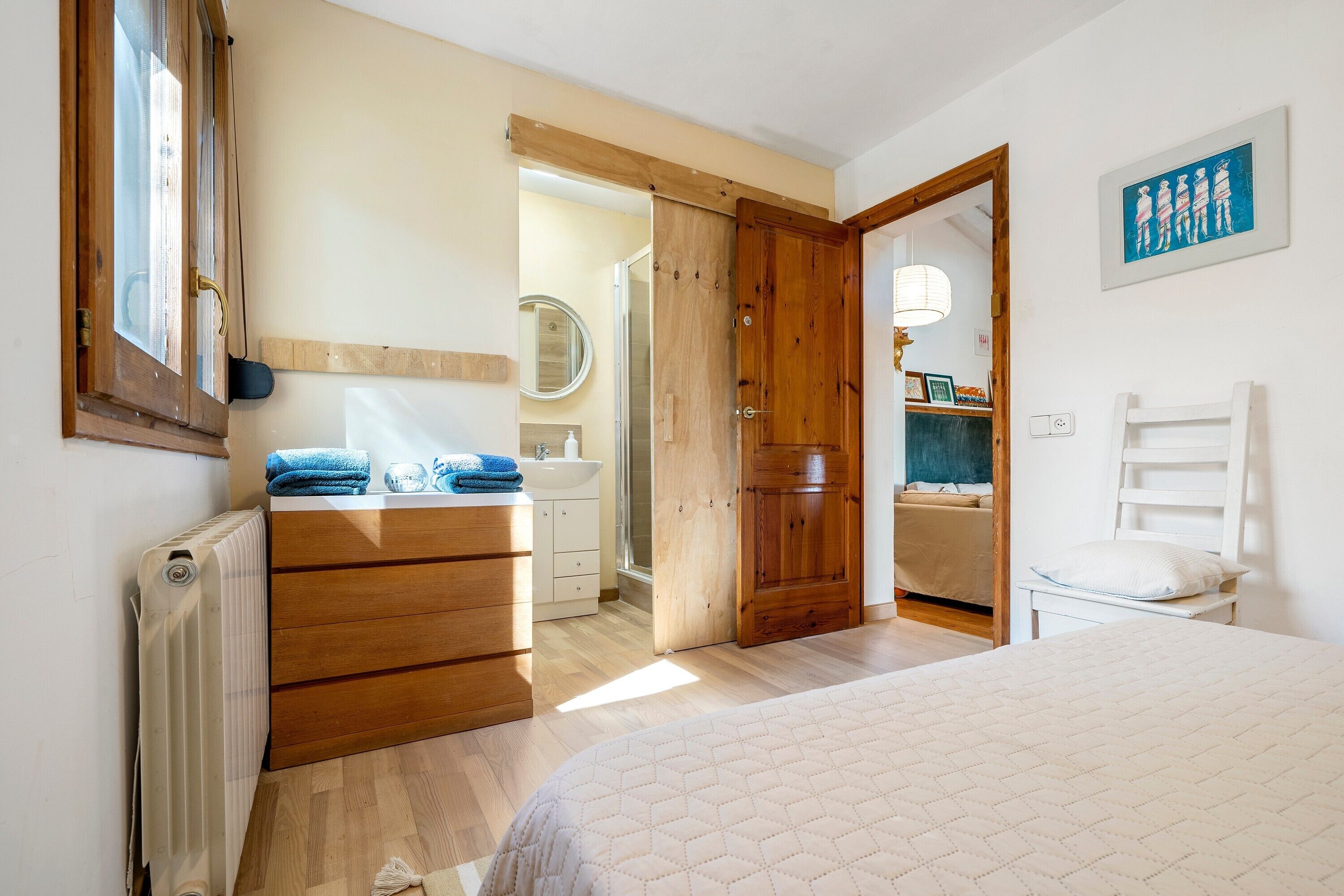 A bedroom with a bed, wooden dresser, and a bathroom visible through an open door.