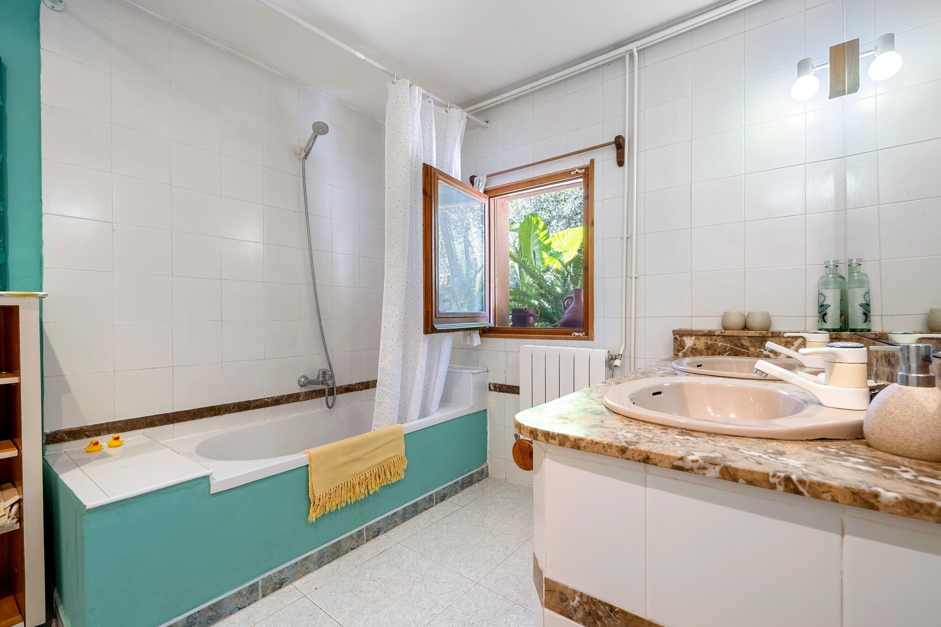 Une salle de bain équipée d’une baignoire, d’une douche, d’un lavabo et d’une fenêtre donnant sur un espace verdoyant.
