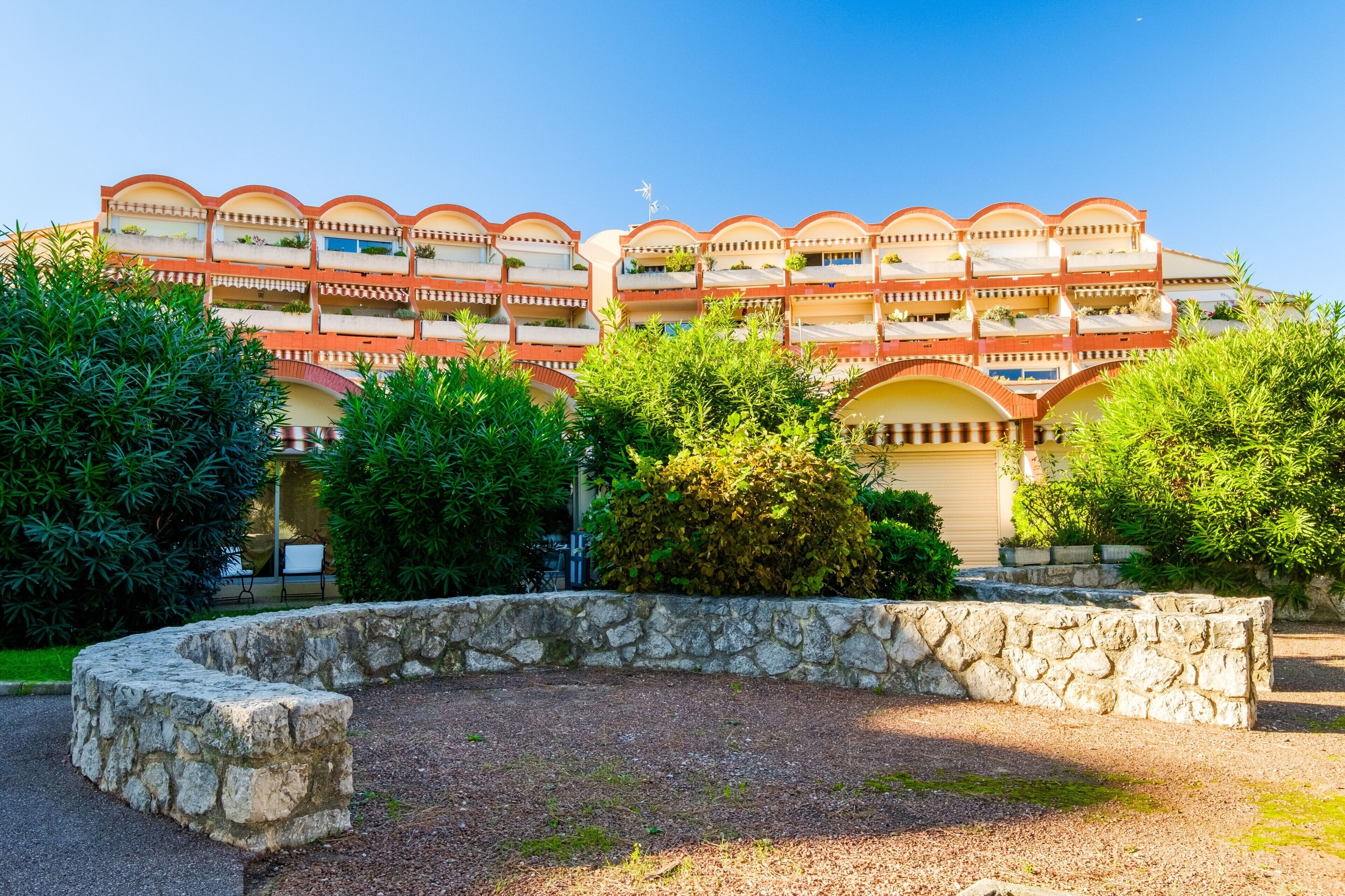 Un hôtel à plusieurs étages, doté de balcons, entouré de verdure et bordé de murs en pierre.