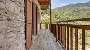 Un balcon en bois avec un mur en pierre, offrant une vue sur une colline boisée.