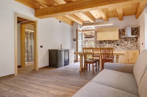 A modern kitchen with wooden cabinets, a dining area with a wooden table and chairs, and a living room with a sofa.
