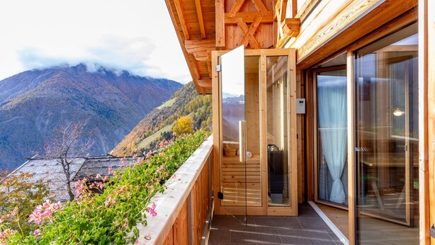 Een houten gebouw met een glazen deur die uitkomt op een balkon met uitzicht op een bergachtig landschap.