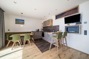 A modern kitchen with a dining area, wooden furniture, and a large TV mounted on the wall. - Apartment 'Waldes Duft - Patleidhof' with Mountain View and Private Sauna on the Balcony (Naturns)
