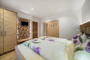 A bedroom with a bed, wooden wardrobe, a wall-mounted TV, and a wooden log wall. - Apartment 'Waldes Duft - Patleidhof' with Mountain View and Private Sauna on the Balcony (Naturns)