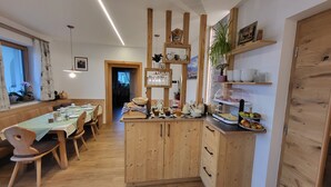 Een eetruimte met houten meubels, een buffet met eten en drinken, en een wand met planken vol borden en kommen.