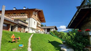 A hillside property with a green lawn, a small slide, and wooden buildings with balconies.