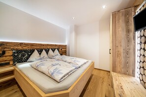Un dormitorio moderno con cabecera de madera, cama con ropa de cama floral, televisor montado en una pared de madera y un banco empotrado.