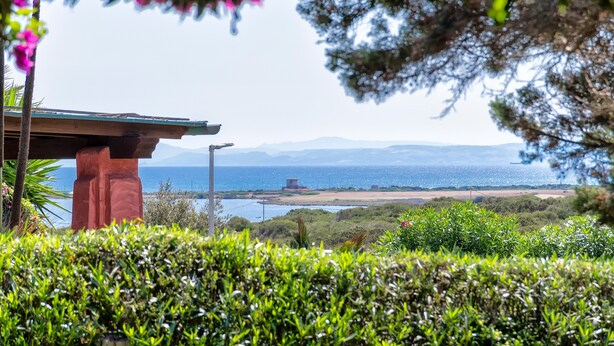 A coastal view with a building, greenery, and a clear sky. - Vacation Home "Villa Robi" near Beach with Private Terrace & Shared Garden (stintino)