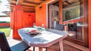 An outdoor dining area with a table set for two, a wooden ceiling, and a view through a glass door. - Vacation Home "Villa Robi" near Beach with Private Terrace & Shared Garden (stintino)