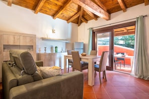 Un espace de vie chaleureux comprenant un canapé, une table à manger avec des chaises, un coin cuisine et une porte-fenêtre coulissante donnant sur une terrasse extérieure.