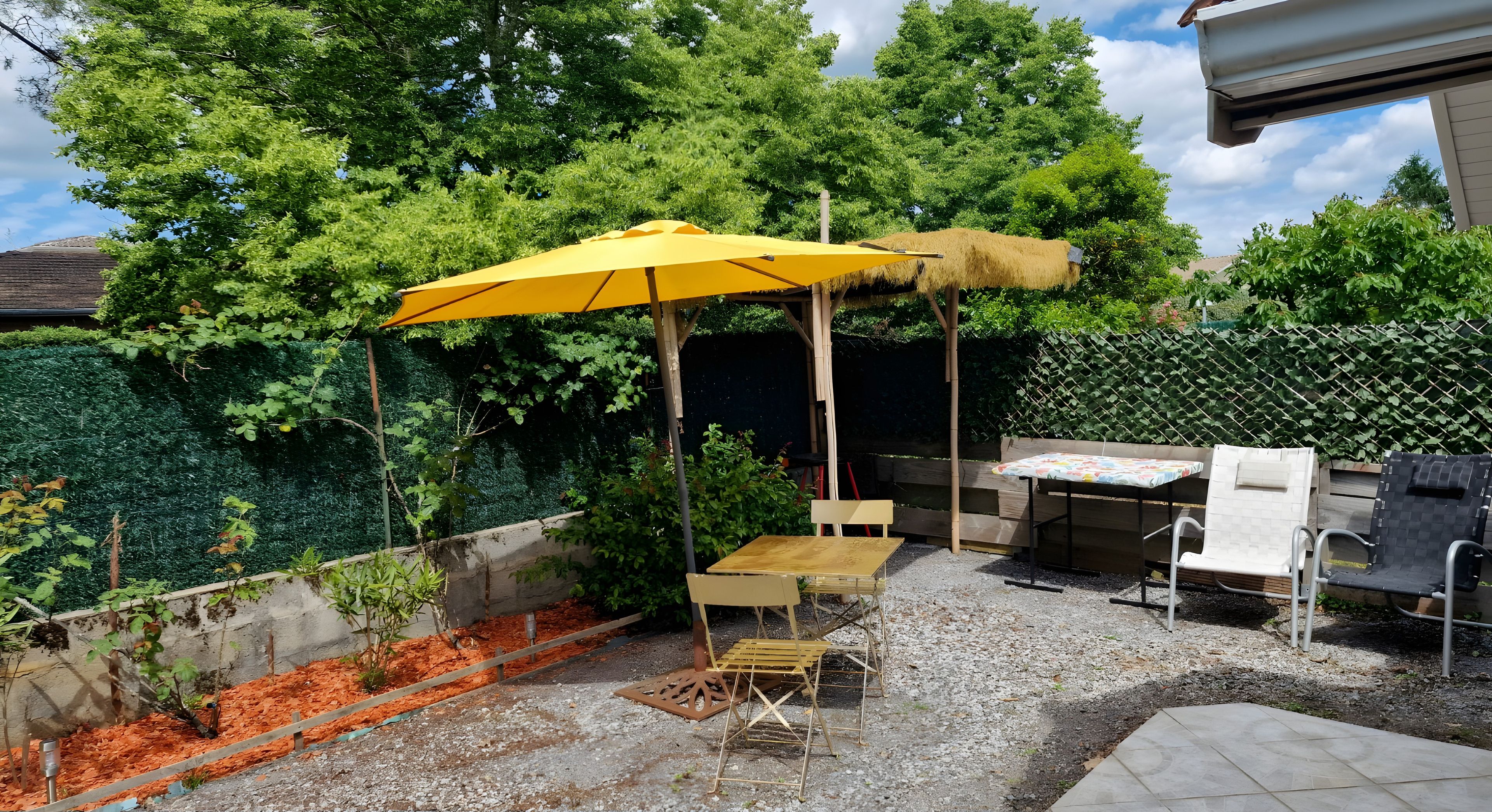 Un espace patio avec un parasol jaune, une table en bois et un barbecue.
