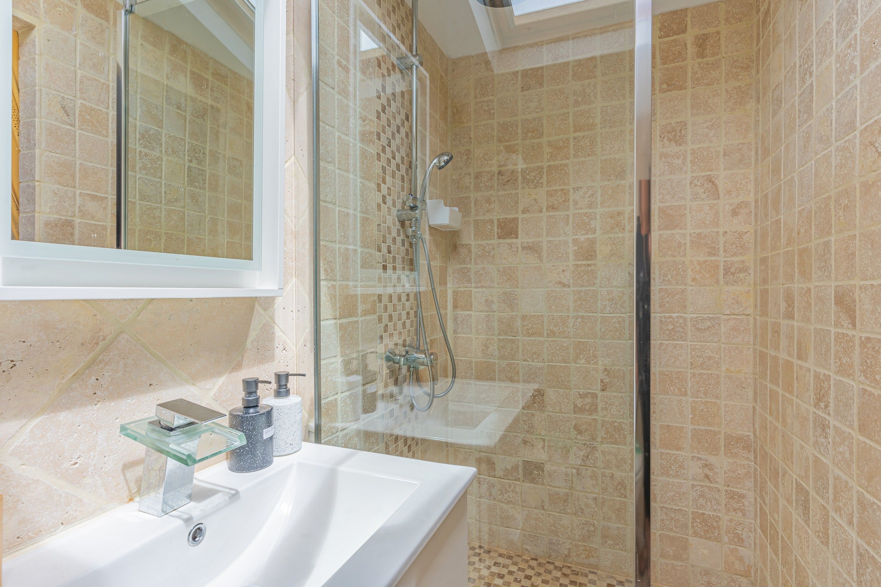 Une salle de bain avec une douche à parois de verre, un lavabo blanc et un miroir au-dessus du lavabo.