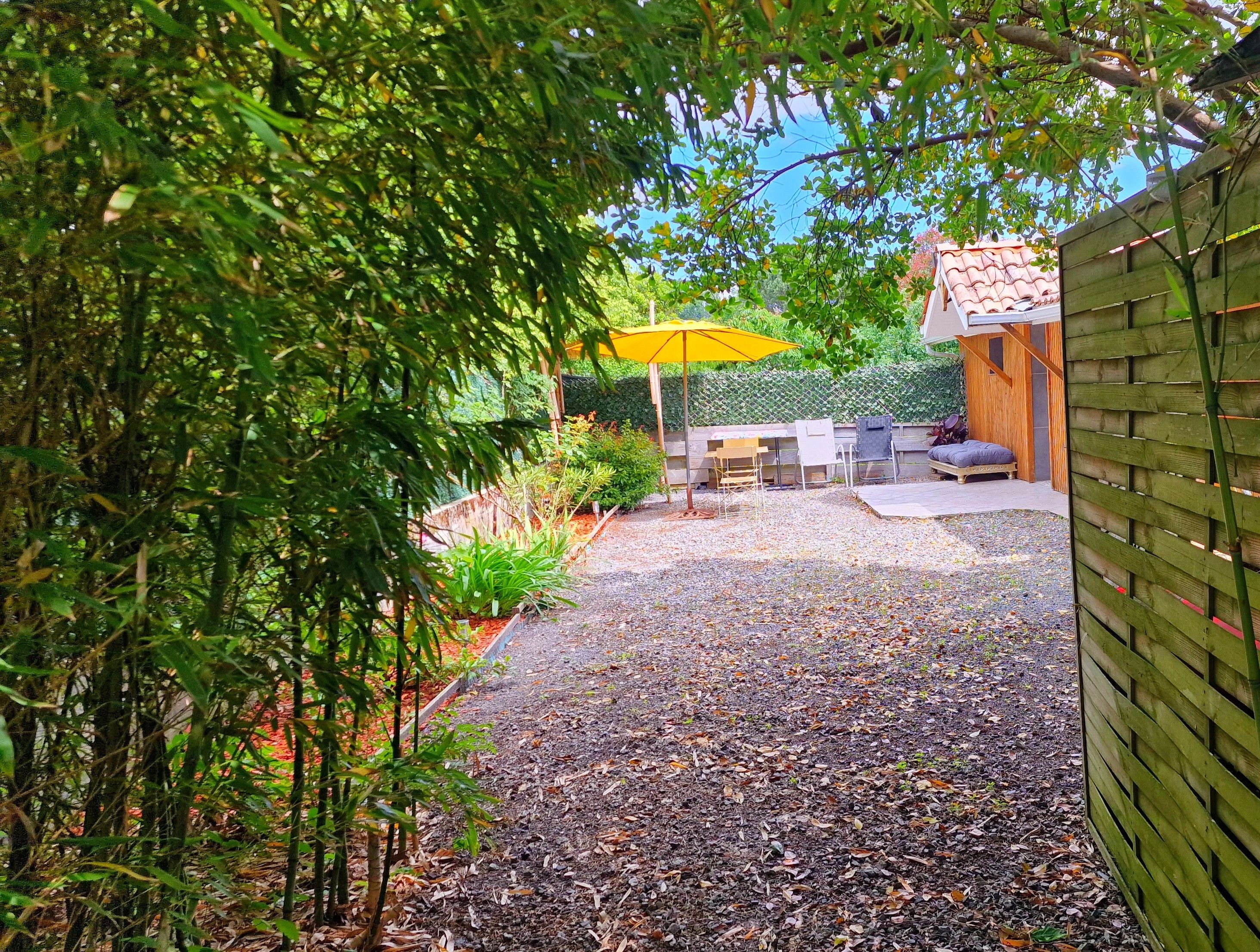 A garden patio with a gravel path, a wooden fence, and a yellow umbrella.