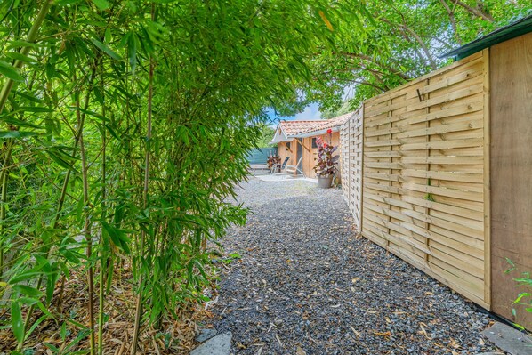 A pathway leading to a building with a tiled roof, surrounded by greenery and a wooden fence.