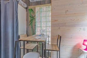 Een kamer met een houten tafel, stoelen, een raam met bamboeblinden en een gordijn.