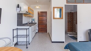 A compact hotel room with a kitchenette, a wooden door, a shower area, and a bed with a blue bedspread. - Spacious 22 m2 Studio in the Village Center n1 (Charleval)