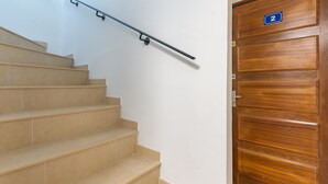 A staircase with a handrail, beige tiled steps, and a wooden door with a number plate. - Spacious 22 m2 Studio in the Village Center n1 (Charleval)