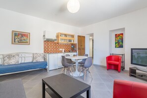 Una sala moderna con un sofá, una mesa de comedor con sillas, un televisor y una zona de cocina con armarios.