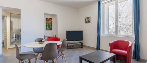 A modern living room with a dining table, chairs, a TV, and a window with curtains.