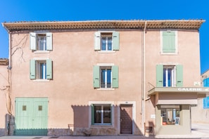 Un bâtiment doté d’une galerie au rez-de-chaussée, de nombreuses fenêtres avec volets et d’une porte.