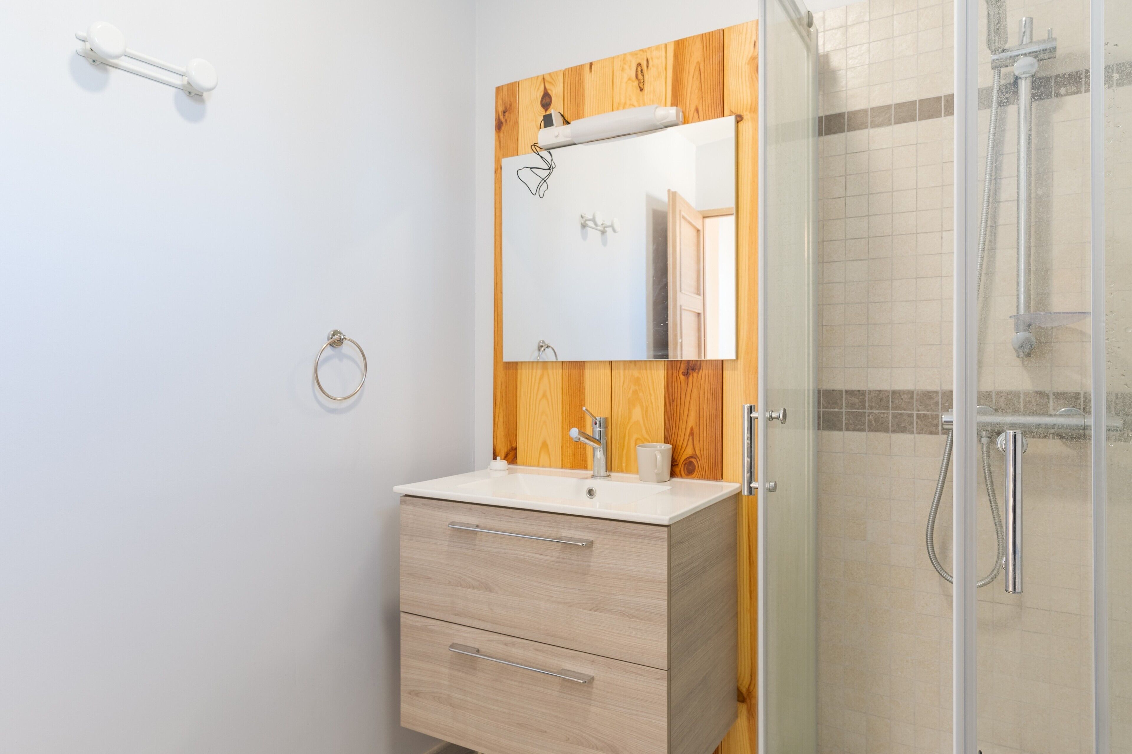 Een badkamer met een houten wastafelmeubel, een spiegel, een wastafel en een douchecabine met glazen wanden.
